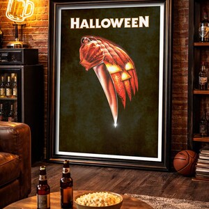 Peut inclure: Une affiche murale rectangulaire encadr&eacute;e avec le mot HALLOWEEN en lettres capitales blanches en haut. Sous le texte se trouve une illustration graphique d'une citrouille lanterne orange tenant un grand couteau de cuisine argent&eacute;.