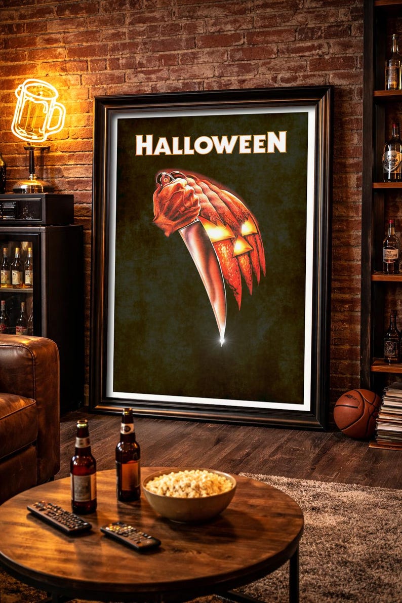 Peut inclure: Une affiche murale rectangulaire encadr&eacute;e avec le mot HALLOWEEN en lettres capitales blanches en haut. Sous le texte se trouve une illustration graphique d'une citrouille lanterne orange tenant un grand couteau de cuisine argent&eacute;.