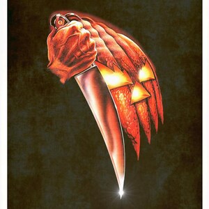 Peut inclure: Une affiche avec le mot HALLOWEEN en texte blanc en haut. En dessous, une citrouille orange textur&eacute;e avec des yeux et une bouche triangulaires lumineux est tenue par une main saisissant un grand couteau de cuisine argent&eacute; sur fond sombre.