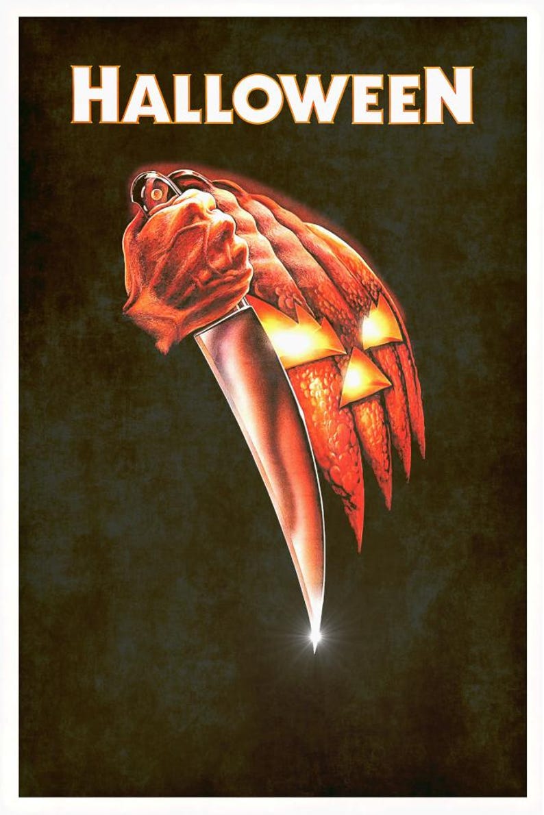 Peut inclure: Une affiche avec le mot HALLOWEEN en texte blanc en haut. En dessous, une citrouille orange textur&eacute;e avec des yeux et une bouche triangulaires lumineux est tenue par une main saisissant un grand couteau de cuisine argent&eacute; sur fond sombre.