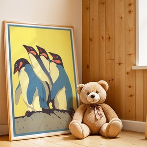 May include: A framed poster featuring a stylized illustration of three penguins with blue, white, and black plumage against a yellow background. A large teddy bear with a brown bow sits nearby. The poster is leaning against a wooden wall.