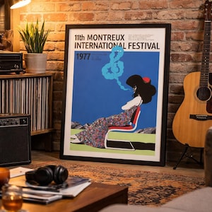 Könnte beinhalten: Gerahmtes Poster für das 11. Montreux International Festival von 1977. Das Kunstwerk zeigt eine Frau in einem Blumenkleid, sitzend, mit einem blauen, rauchartigen Design. Das Poster befindet sich in einem Raum mit einer Gitarre und einer Backsteinmauer.