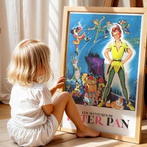 Op de afbeelding: Een ingelijste poster met de titel "Les Aventures de Peter Pan" in roze. De illustratie toont Peter Pan in een gele outfit, omringd door andere personages. Een jong kind zit op de grond en bekijkt de poster.