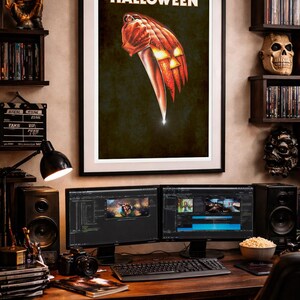Peut inclure: Une affiche murale encadr&eacute;e intitul&eacute;e HALLOWEEN pr&eacute;sentant une illustration graphique d'une t&ecirc;te de citrouille orange sculpt&eacute;e aux yeux brillants tenant un grand couteau de cuisine argent&eacute; sur un fond sombre et textur&eacute;.