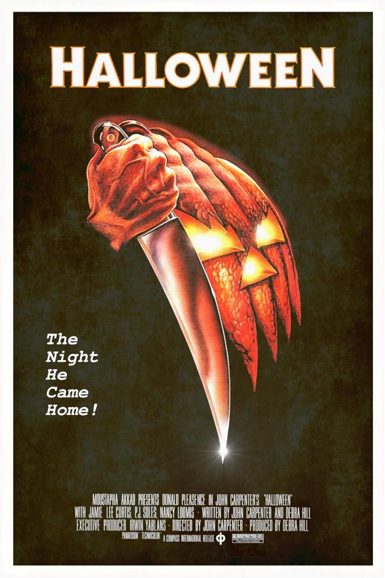 Peut inclure: Une affiche de film pour Halloween repr&eacute;sentant une grande citrouille orange sculpt&eacute;e avec des yeux et une bouche lumineux, tenue par une main agrippant un couteau argent&eacute;. Le texte indique HALLOWEEN, The Night He Came Home!, et les cr&eacute;dits.