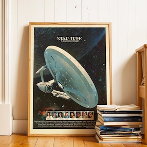 Puede incluir: Póster enmarcado de Star Trek: La Película. La obra de arte presenta la U.S.S. Enterprise en el espacio sobre un fondo azul oscuro y negro. El póster está en un marco de madera y está apoyado contra una pared blanca.
