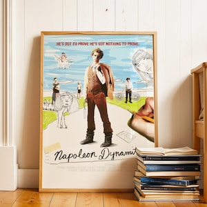 May include: A framed poster for the film "Napoleon Dynamite", showing a man in a brown suit. The poster includes the text "HE'S OUT TO PROVE HE'S GOT NOTHING TO PROVE". The poster is leaning against a white wall, with a stack of books in front.