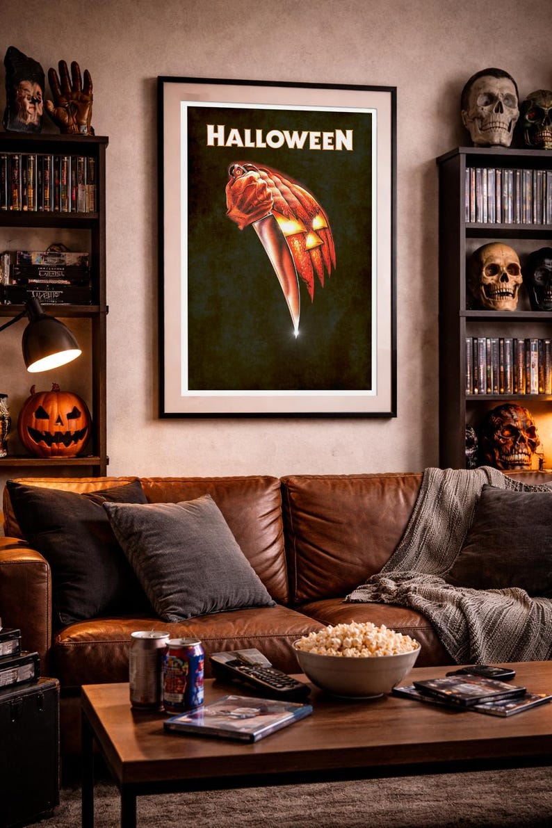 Peut inclure: Une affiche murale encadr&eacute;e pr&eacute;sentant le mot HALLOWEEN en lettres blanches au-dessus d'une illustration d'une main tenant un grand couteau de cuisine, dont la lame se transforme en citrouille illumin&eacute;e sur un fond sombre.