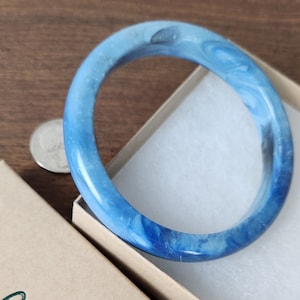 Könnte beinhalten: Ein blaues und weißes Swirl-Armband. Das Armband ist aus einem glatten, polierten Material gefertigt und hat ein schlichtes, elegantes Design.