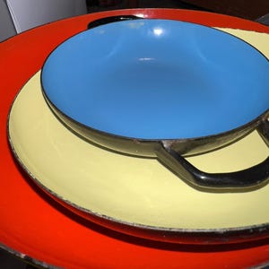 May include: Three nesting cookware pieces with a red, yellow, and blue enamel finish. The largest piece is red, the middle piece is yellow, and the smallest piece is blue. The blue piece has two black handles.