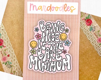 May include: Pink sticker with the text "Being Nice is the Bare Minimum" in a retro font. The sticker is decorated with flowers and smiley faces.