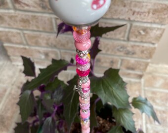 May include: A pink and white ceramic garden stake with a heart design. The stake is decorated with pink, white, and clear beads.
