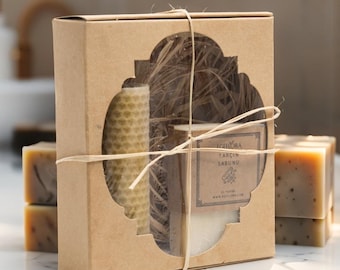 May include: A gift set in a brown cardboard box tied with twine. The box has a decorative window revealing a honeycomb candle, a bar of soap, and dried plant material. Several bars of soap are visible.
