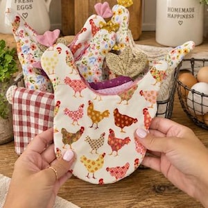 May include: A fabric chicken-shaped pot holder featuring a repeating pattern of colorful chickens in shades of red, orange, yellow, and brown on an off-white background, with a small pink fabric comb detail at the top of the head.