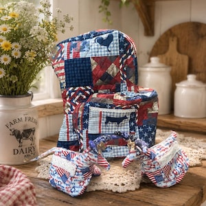 Könnte beinhalten: Eine gesteppte Geräteabdeckung aus Stoff und zwei passende Ofenhandschuhe mit einem Patchwork-Design in Rot, Weiß und Blau. Die Abdeckung zeigt eine dunkelblaue Kuh-Silhouette auf einer Vordertasche, während die Handschuhe ein patriotisches Sternenmuster haben.