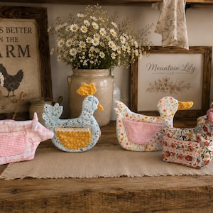 May include: Four fabric animal-shaped organizers featuring a pig, a chicken, a duck, and a horse. Each figure is crafted from patterned cotton fabric with a small pocket on the side, showcasing floral, gingham, and botanical prints in soft pastel colors.