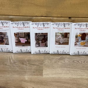 May include: Five white rectangular instruction booklets titled The Farmhouse Collection Potholders by Mountain Lily Designs. Each booklet features a unique photograph of a fabric animal-shaped potholder and decorative botanical line art borders.