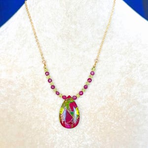 May include: A gold chain necklace featuring a teardrop-shaped pendant with a multicolored mosaic pattern in shades of magenta, lime green, and gold. The chain is accented with small, alternating round magenta and lime green faceted beads.