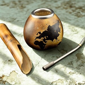 Puede incluir: Un juego de yerba mate con una calabaza con un diseño de mapa del mundo, una pajita de bambú y una bombilla de metal. La calabaza es marrón con un borde plateado. La pajita de bambú es marrón claro.