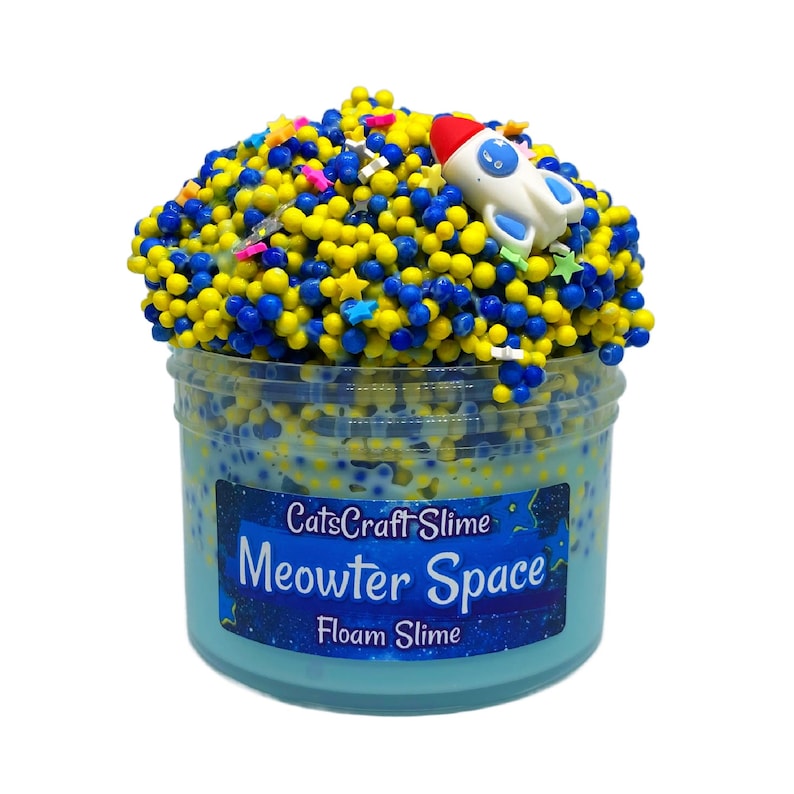 May include: A clear plastic container filled with blue, yellow, and white foam slime. The slime is topped with yellow and blue beads, star-shaped sprinkles, and a small white rocket ship. The container has the text "CatsCraft Slime Meowter Space Foam Slime".
