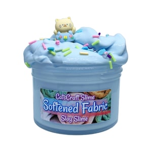 May include: A jar of light blue slime with colorful sprinkles and a small cat figurine on top. The jar has a label that reads "CatsCraft Slime Softened Fabric Slay Slime."