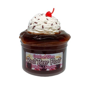May include: A clear jar of brown slime with a white whipped cream topping and a red cherry on top. The jar has a label that says "CatsCraftSlime Root Beer Float DIY Clay / Jelly Slime".