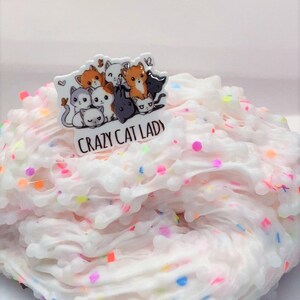 May include: White fluffy slime with colorful sprinkles and a charm of a group of cartoon cats with the text "Crazy Cat Lady".