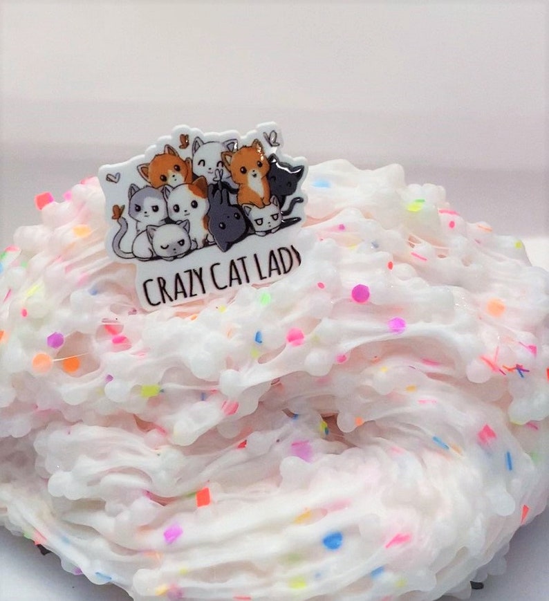 May include: White fluffy slime with colorful sprinkles and a charm of a group of cartoon cats with the text "Crazy Cat Lady".