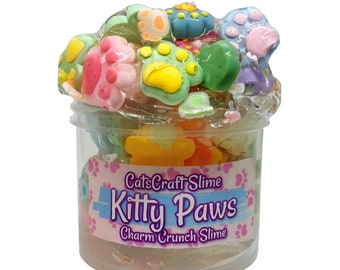 May include: A clear plastic container filled with a light pink slime with colorful paw print charms. The container has a label that reads "CatsCraft Slime Kitty Paws Charm Crunch Slime".