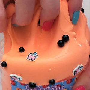 Pu&ograve; includere: Slime denso e lucido alla pesca Boba di CuisCraft Slime. Lo slime &egrave; di colore arancione brillante con palline di boba nere e fette di pesca sull'etichetta.