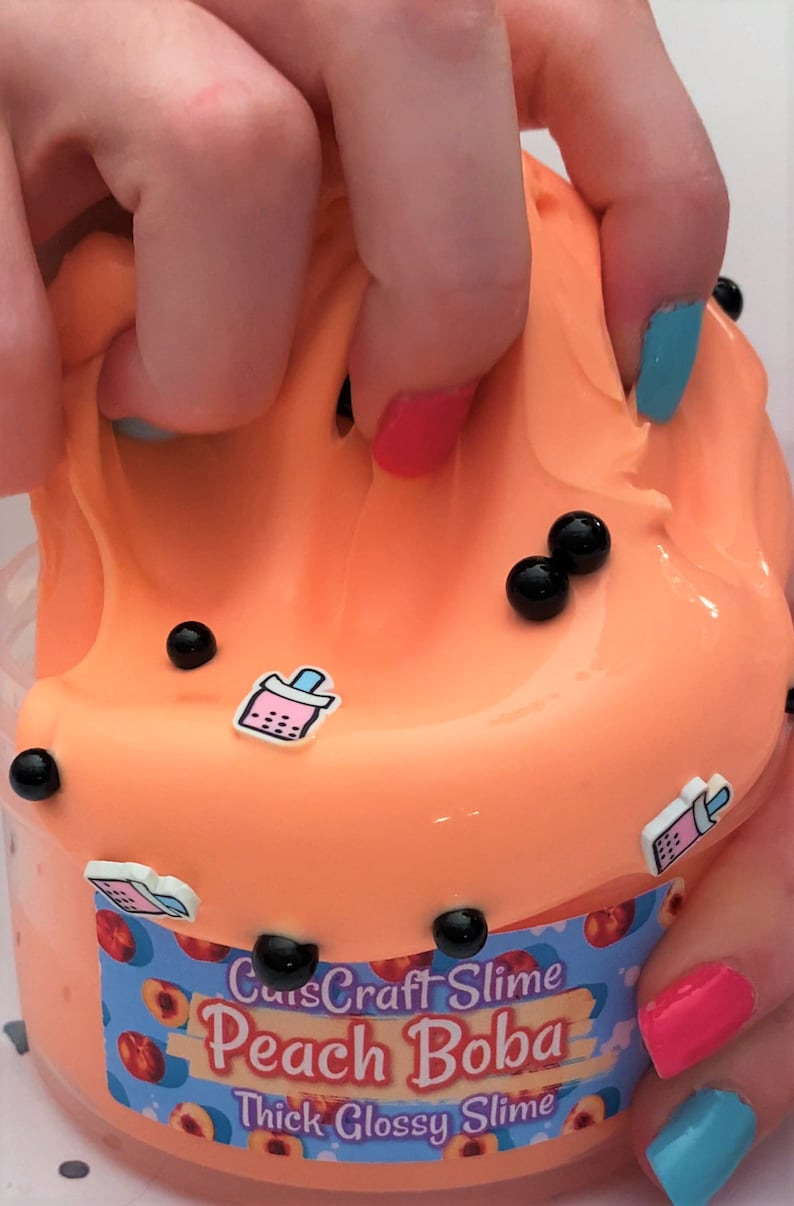 Pu&ograve; includere: Slime denso e lucido alla pesca Boba di CuisCraft Slime. Lo slime &egrave; di colore arancione brillante con palline di boba nere e fette di pesca sull'etichetta.