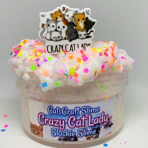 May include: A clear jar filled with white slushie slime with colorful glitter and sprinkles. The jar has a label that reads "CatsCraft Slime Crazy Cat Lady Slushie Slime". A charm with a group of cartoon cats is on top of the jar.