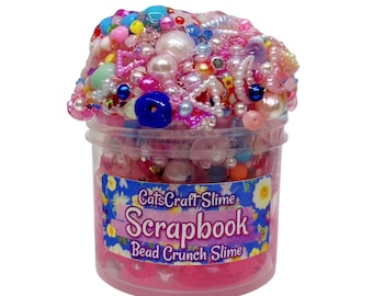 May include: A pink slime with a variety of colorful beads and pearls in a clear plastic jar. The jar has a label that reads "CatsCraft Slime Scrapbook Bead Crunch Slime".