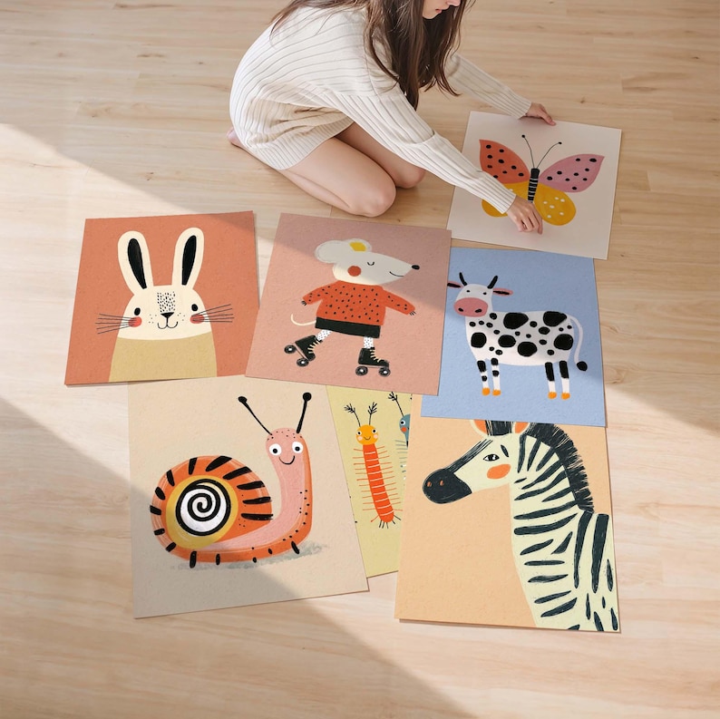 May include: A collection of colorful animal illustrations on square cards. The images include a rabbit, mouse on roller skates, butterfly, cow, snail, caterpillar, and zebra. The cards are arranged on a light-colored wooden floor.