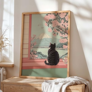 May include: A framed art print featuring a black and gray striped cat gazing out a window at a mountain landscape. The scene includes pink cherry blossoms, a vase, and a traditional Japanese aesthetic. The frame is made of light-colored wood.
