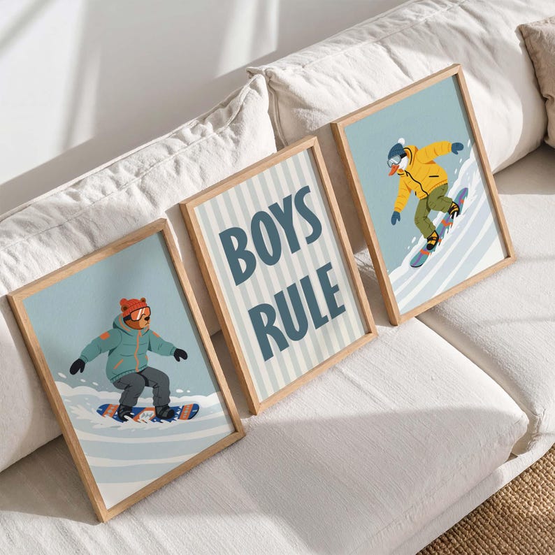 May include: Three framed art prints featuring illustrations of snowboarders and the text "BOYS RULE." The prints have light blue backgrounds and wooden frames. The snowboarders are wearing winter gear in shades of blue, yellow, and orange.