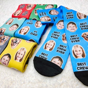 May include: A set of colorful socks with different designs. Some socks feature the text "Best Crew Ever" and others feature the text "We Love Dad" and "#1 Dad".  The socks have a variety of images of people and animals.