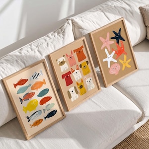 May include: Three framed art prints featuring colorful illustrations. One print showcases various fish, another features dog breeds, and the third displays starfish and a seashell. Each print is in a light wood frame, creating a cohesive set for wall decor.