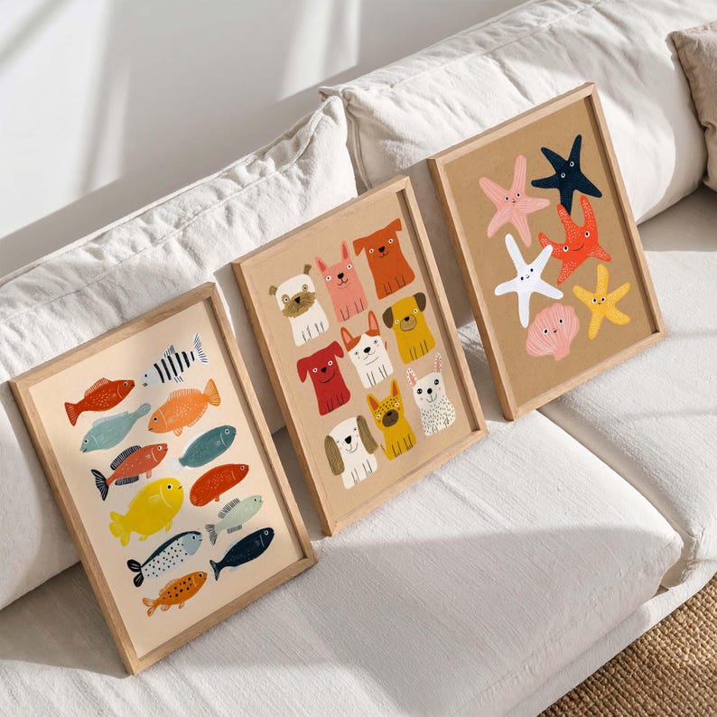 May include: Three framed art prints featuring colorful illustrations. One print showcases various fish, another features dog breeds, and the third displays starfish and a seashell. Each print is in a light wood frame, creating a cohesive set for wall decor.