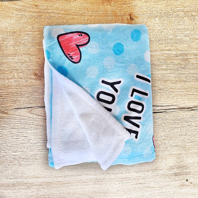 May include: A blue fleece blanket with white polka dots and a red heart. The blanket has the words "I love you" printed on it.