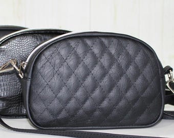 May include: A collection of small, crossbody bags in various colors. The bags are black, blue, and black with a crocodile texture. The front-most bag is black with a quilted pattern. Each bag has a silver zipper and strap.