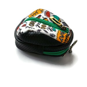 K&ouml;nnte beinhalten: Eine kleine, schwarze und wei&szlig;e Rei&szlig;verschlusstasche mit einem gr&uuml;nen Rei&szlig;verschluss. Die Tasche hat ein schwarz-wei&szlig;es Punkte-Muster und den Text "Good Day" auf der Vorderseite.