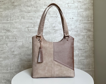Könnte beinhalten: Eine beige und braune Tragetasche mit einem Quastenanhänger. Die Tasche hat ein geometrisches Design und ist aus Kunstleder.