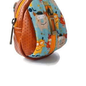 K&ouml;nnte beinhalten: Ein kleiner, brauner und blauer Rucksack mit Rei&szlig;verschluss. Der Rucksack hat einen Cartoon-Monster-Druck mit dem Wort "COOL" darauf.