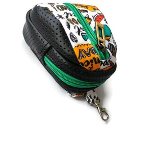 K&ouml;nnte beinhalten: Eine kleine schwarze und wei&szlig;e Rei&szlig;verschlusstasche mit einem gr&uuml;nen Rei&szlig;verschluss und einem goldenen Verschluss. Die Tasche hat ein schwarz-wei&szlig;es Punkte-Muster und die W&ouml;rter "Adventure" und "Everyday" sind darauf gedruckt. Die Tasche hat einen kleinen Metallring.