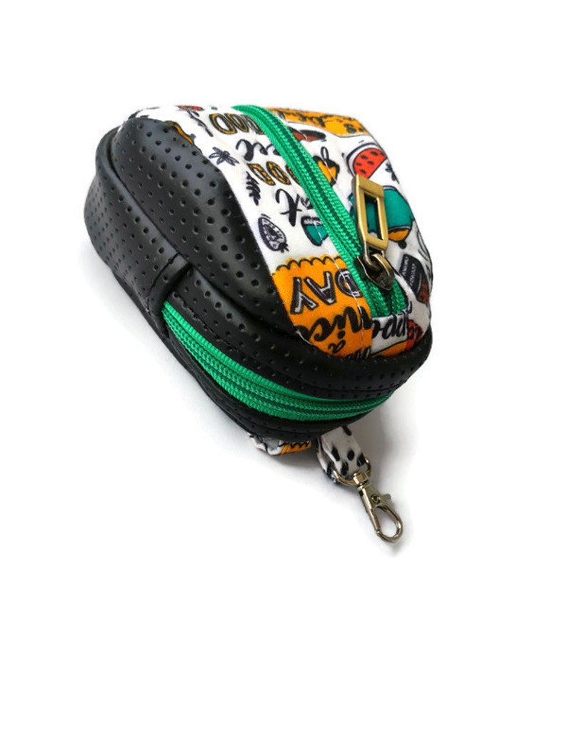 K&ouml;nnte beinhalten: Eine kleine schwarze und wei&szlig;e Rei&szlig;verschlusstasche mit einem gr&uuml;nen Rei&szlig;verschluss und einem goldenen Verschluss. Die Tasche hat ein schwarz-wei&szlig;es Punkte-Muster und die W&ouml;rter "Adventure" und "Everyday" sind darauf gedruckt. Die Tasche hat einen kleinen Metallring.