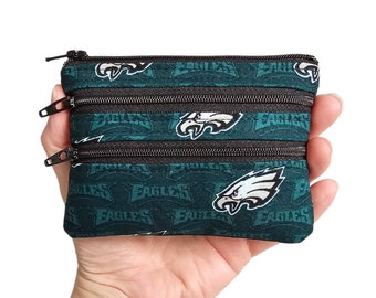 May include: A small green and black zippered pouch with a repeating pattern of the Philadelphia Eagles logo and the word "Eagles".
