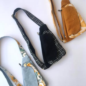 Puede incluir: Tres bolsos de bandolera diferentes con varios patrones. El primer bolso es negro con patrones geométricos blancos, el segundo es azul claro con un patrón floral y el tercero es amarillo mostaza con un patrón blanco.