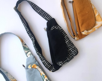 May include: Three different crossbody bags with various patterns. The first bag is black with white geometric patterns, the second is light blue with a floral pattern, and the third is mustard yellow with a white pattern.