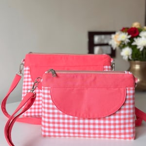 May include: Two rectangular crossbody bags featuring a vibrant coral pink solid fabric top panel and a white and coral pink gingham checkered pattern on the lower section. Each bag includes a matching coral pink flap and a silver zipper closure.